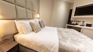 Una habitación de hotel moderna con una cama grande, una mesita de noche, un televisor de pantalla plana montado en la pared y un pequeño escritorio con una cafetera.