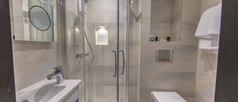 A modern bathroom with a glass-enclosed shower, a white sink, and a toilet.