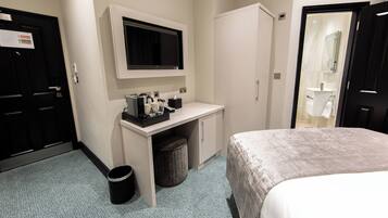 A hotel room with a bed, a desk with a TV, a mirror, and a small trash bin.