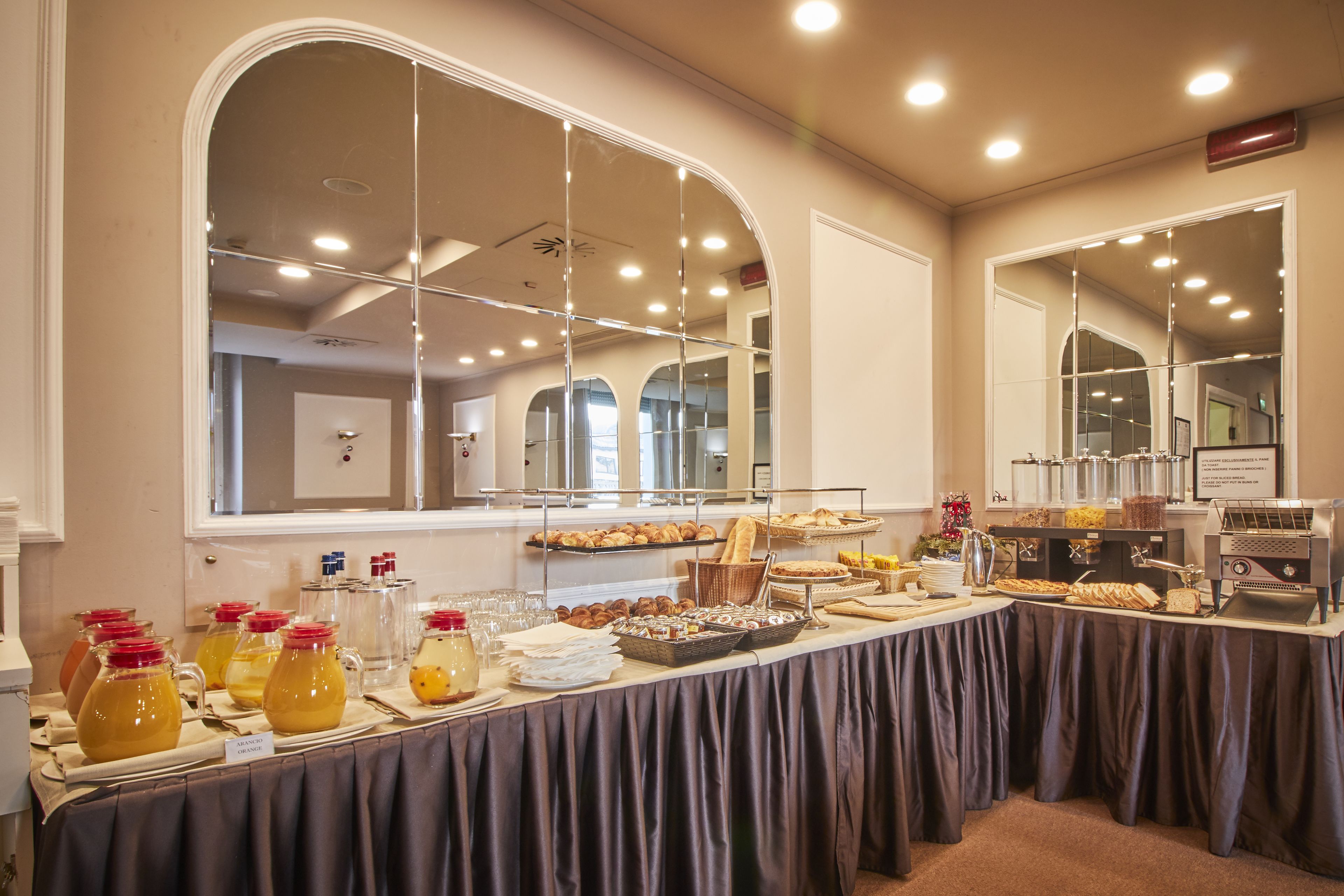A buffet setup with various food items and beverages, a coffee machine, and a large mirror reflecting the room.