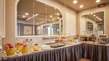 Tavolo del buffet con diversi cibi e bevande, una macchina del caffè e un grande specchio che riflette l'ambiente.