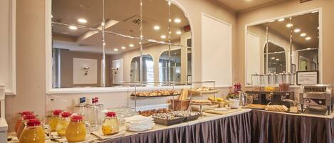 A buffet setup with various food items and beverages, a coffee machine, and a large mirror reflecting the room.