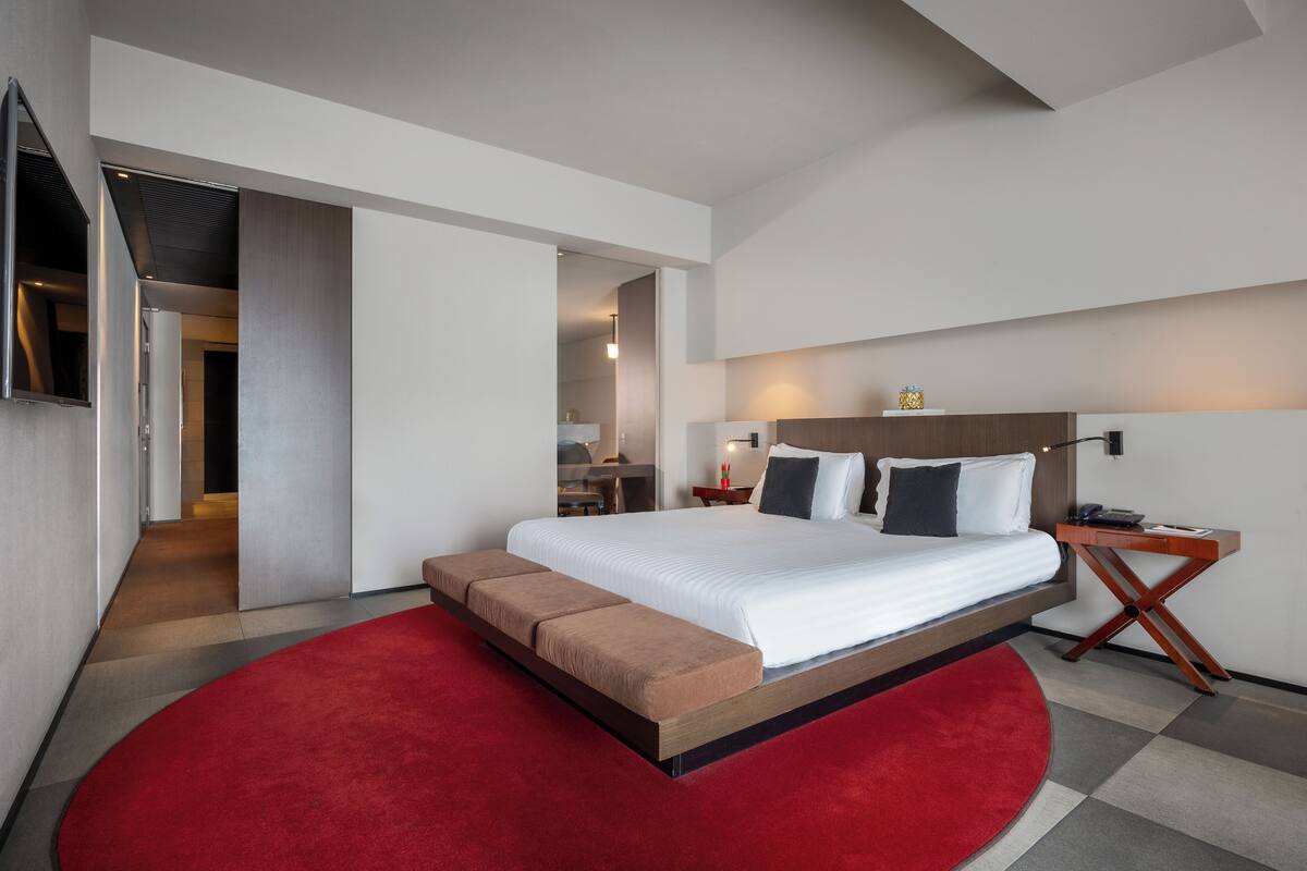 A modern hotel room with a large bed, a red carpet, and a wooden nightstand.