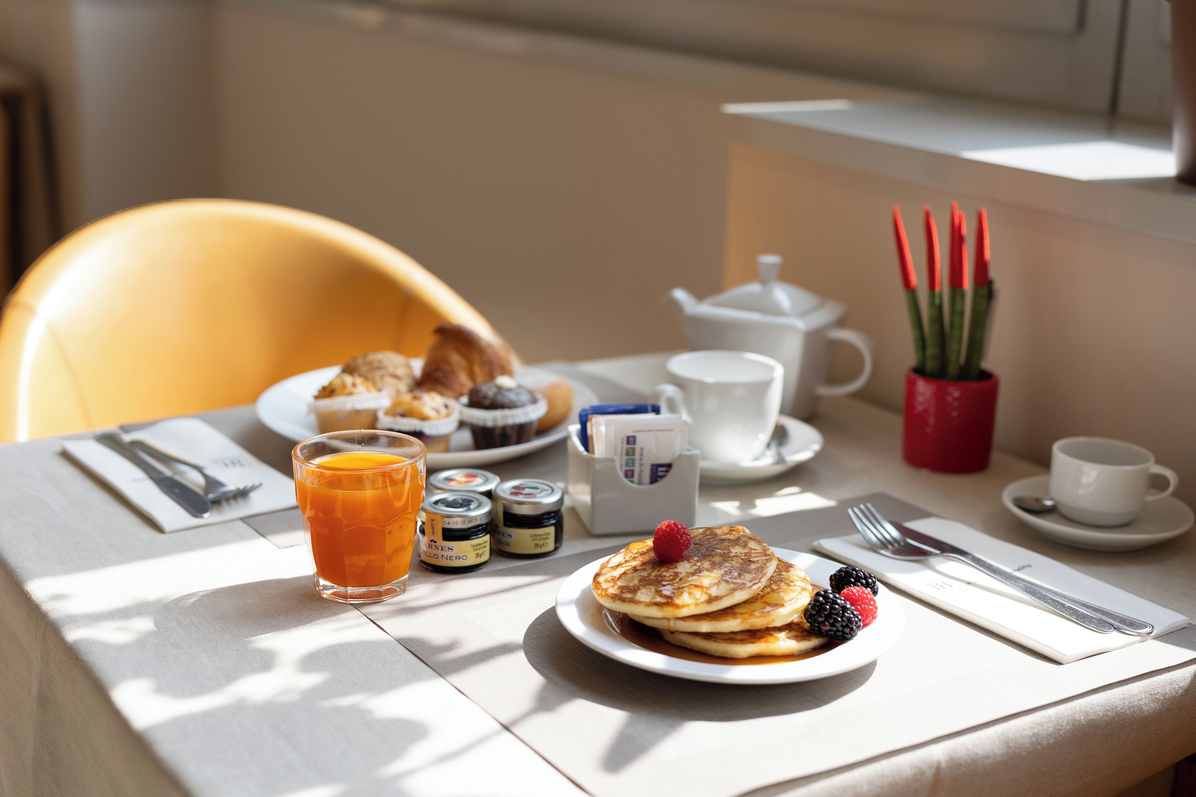 Ett frukostbord med pannkakor, bär, ett glas apelsinjuice och olika tillbehör.