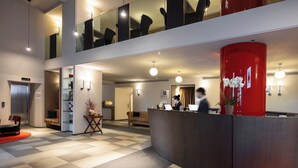 A modern hotel lobby with a check-in counter, seating area, and a staircase leading to an upper level. - iH Hotels Milano Ambasciatori (Milan)