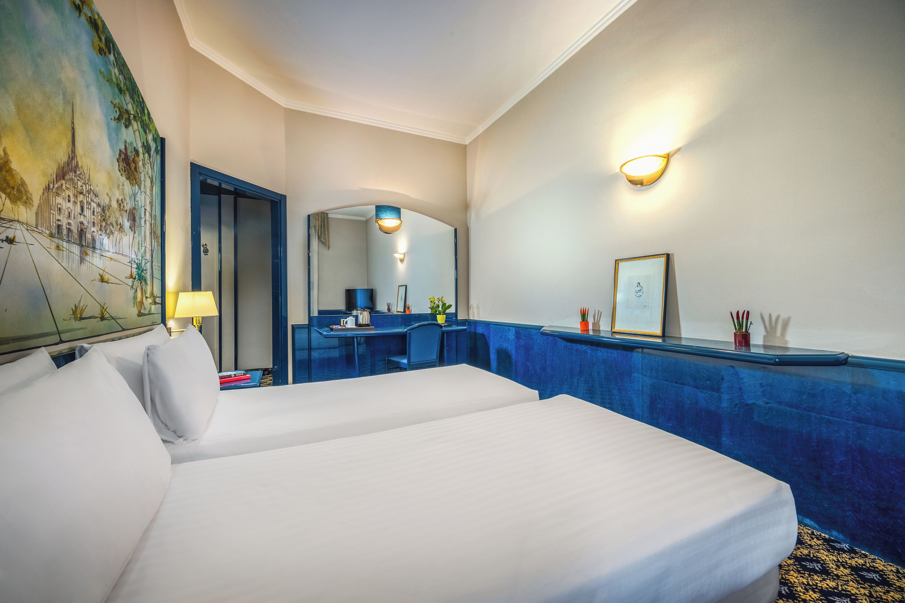 Une chambre d’hôtel avec deux lits, un bureau, un miroir et un tableau au mur.