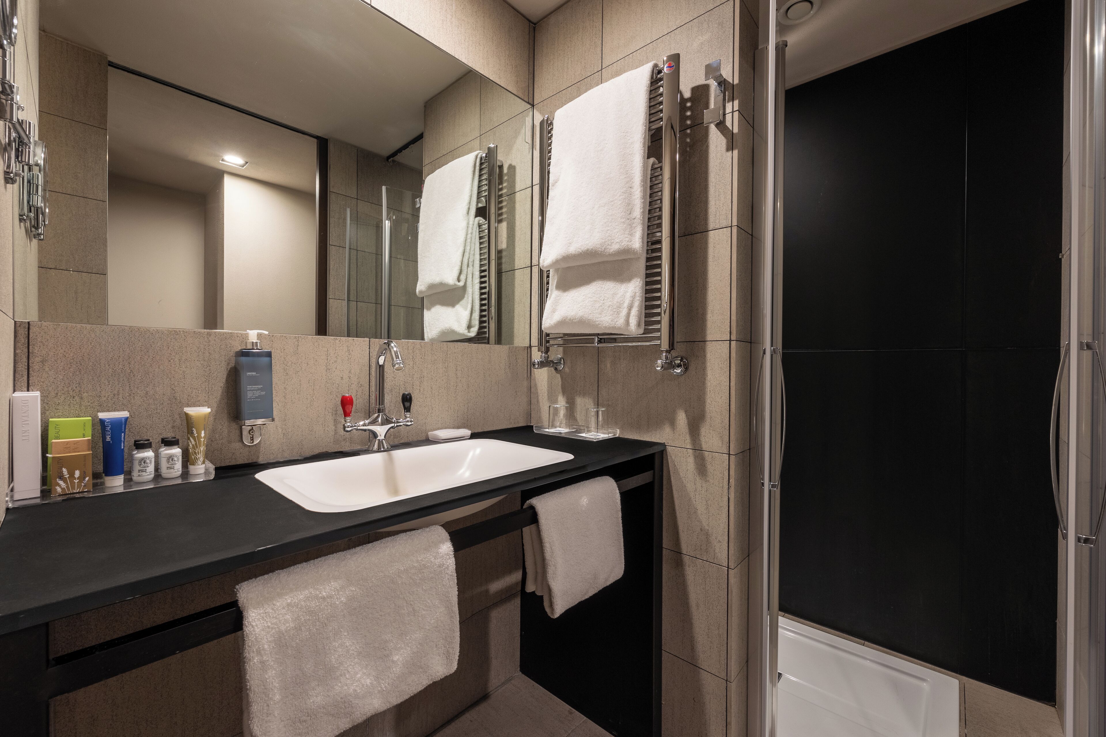 Une salle de bain moderne avec un plan de toilette noir, un lavabo blanc et une cabine de douche en verre.