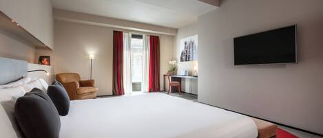 A hotel room with a large bed, a desk, a chair, a TV, and a window with curtains.