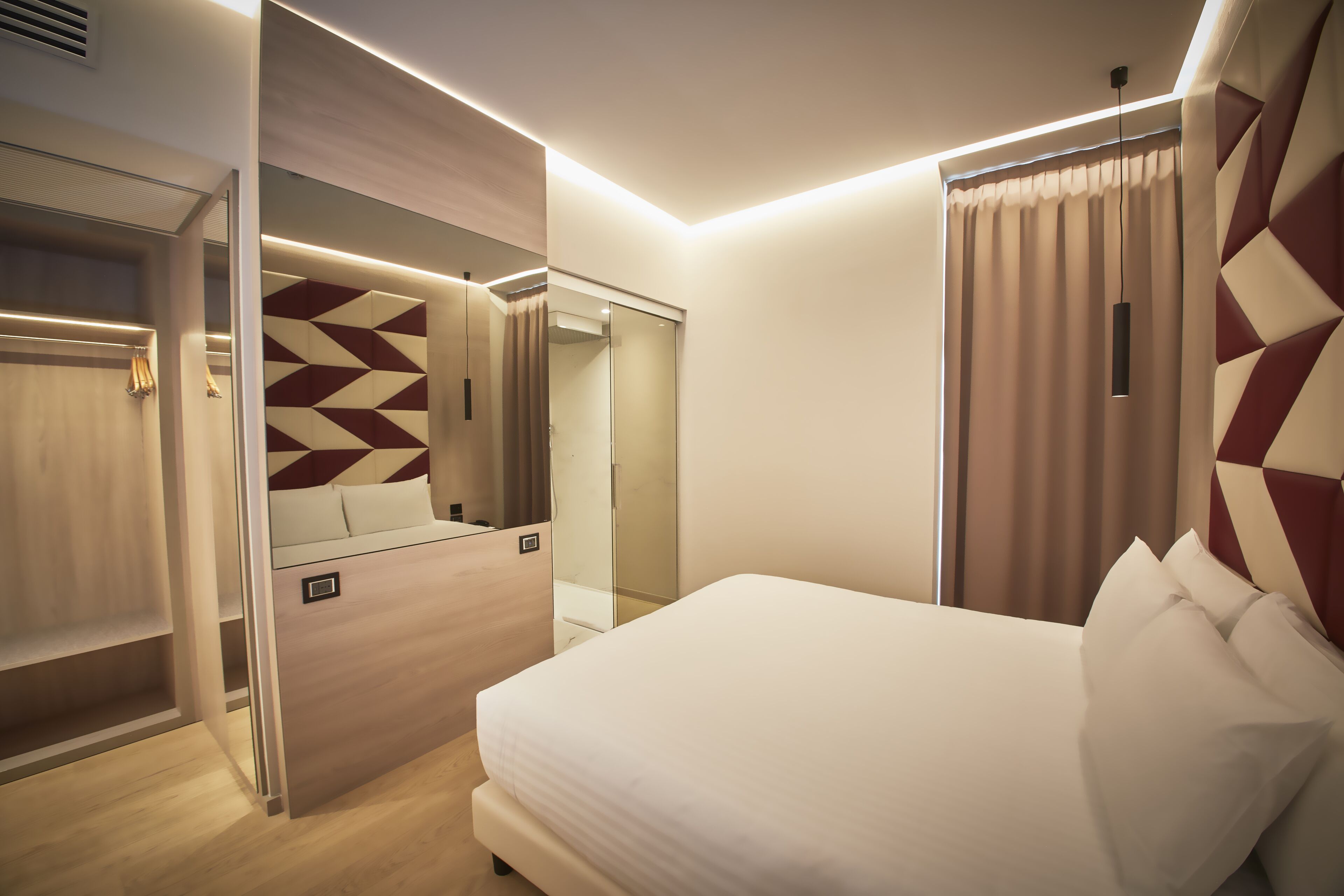 A modern hotel room with a bed, a wardrobe, a mirror, and a geometric-patterned wall.