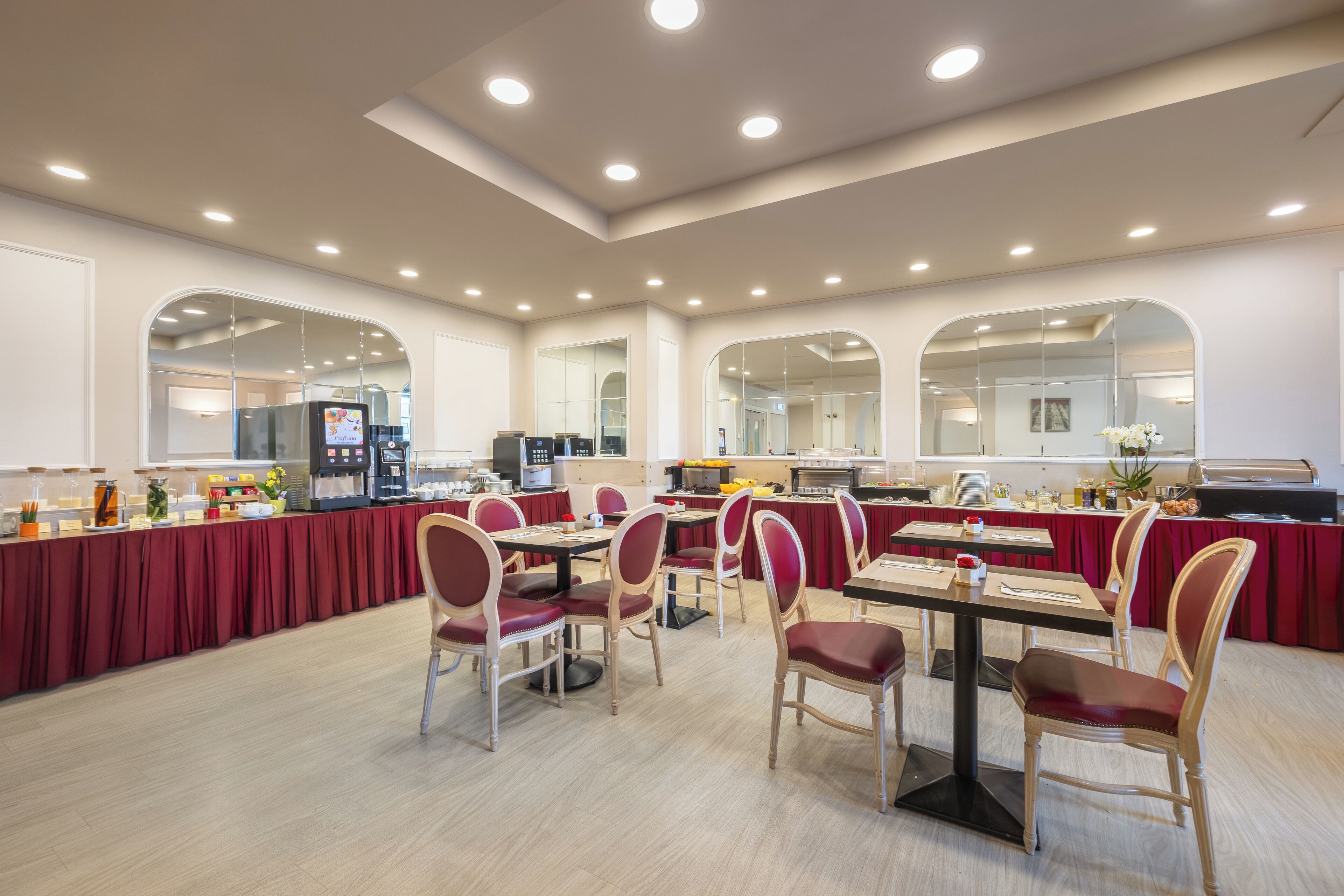 Un espace repas moderne avec des tables et des chaises rondes, un buffet et une cuisine en arrière-plan.