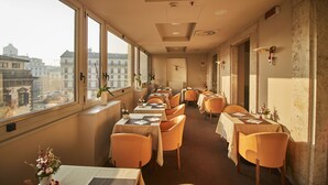 A hotel room with large windows, a view of the city, and a long corridor with tables and chairs. - iH Hotels Milano Ambasciatori (Milan)