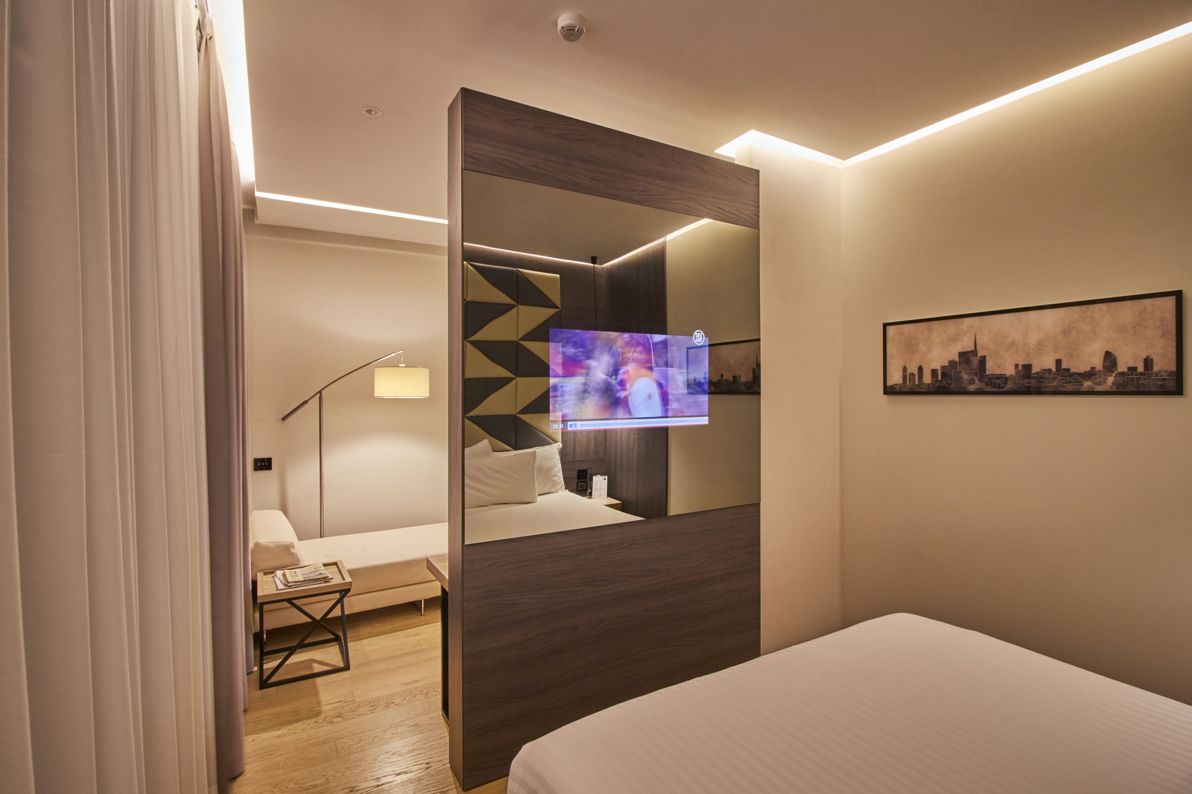 Una habitación de hotel moderna con cama, escritorio, silla, televisor y una pintura de paisaje urbano.