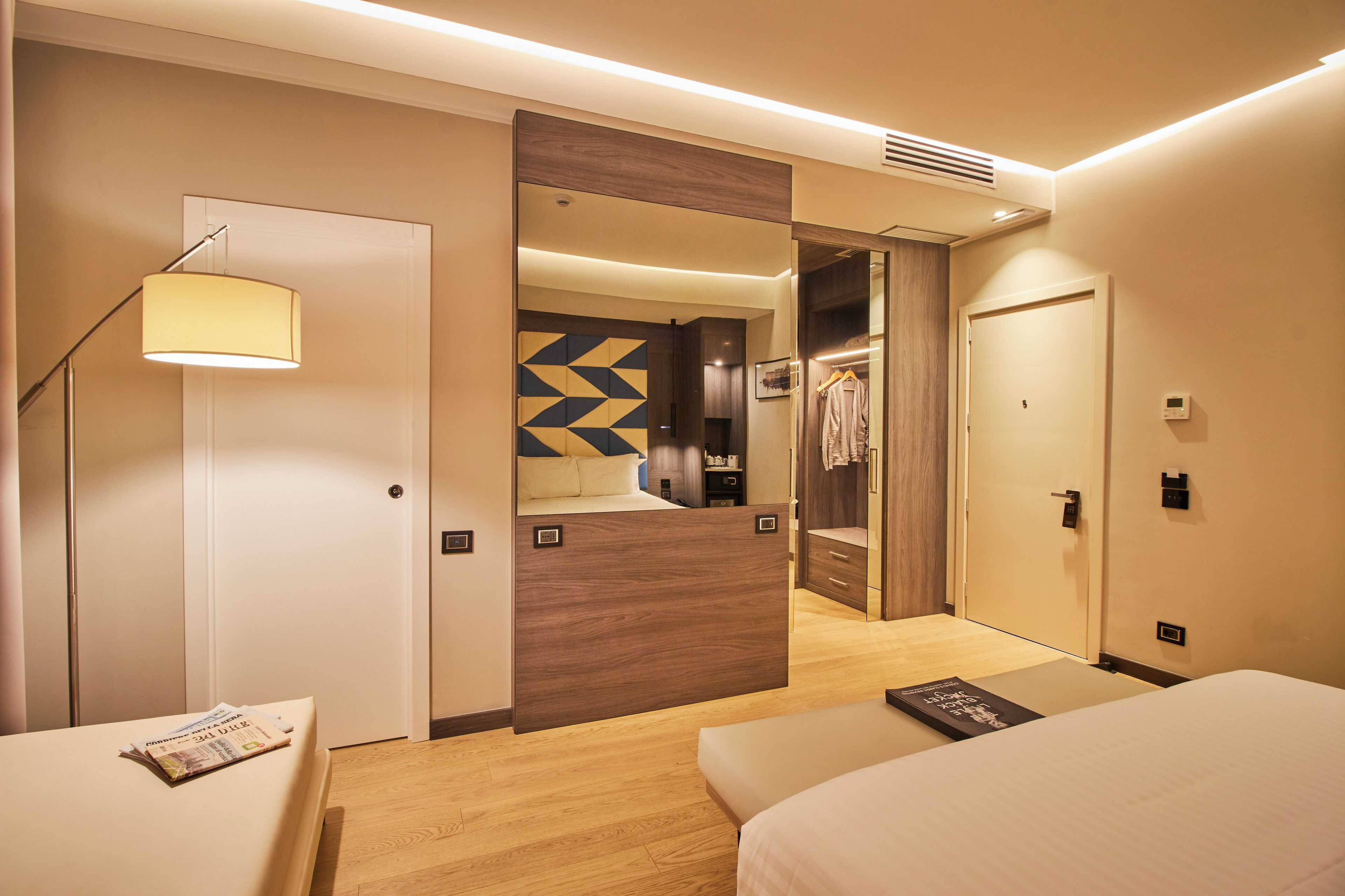 Una habitación de hotel con cama, mesita de noche, lámpara, armario y espejo.
