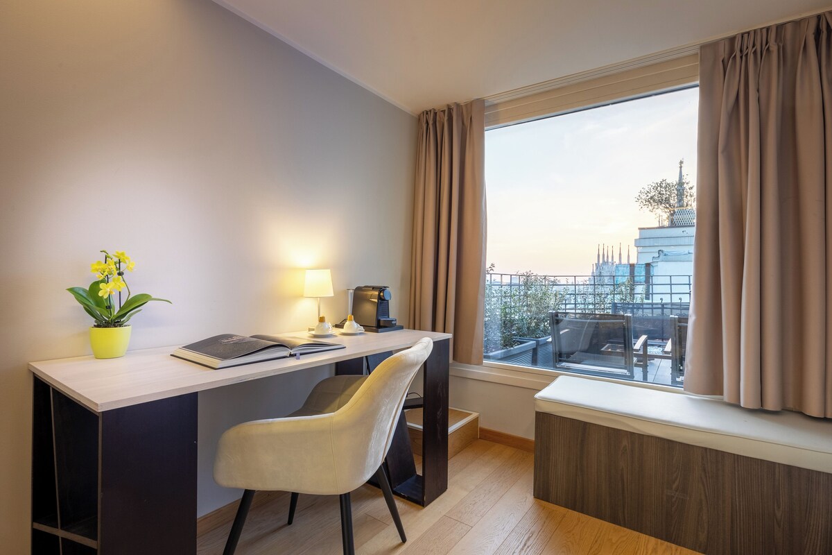 A modern hotel room with a desk, chair, and a large window with curtains.
