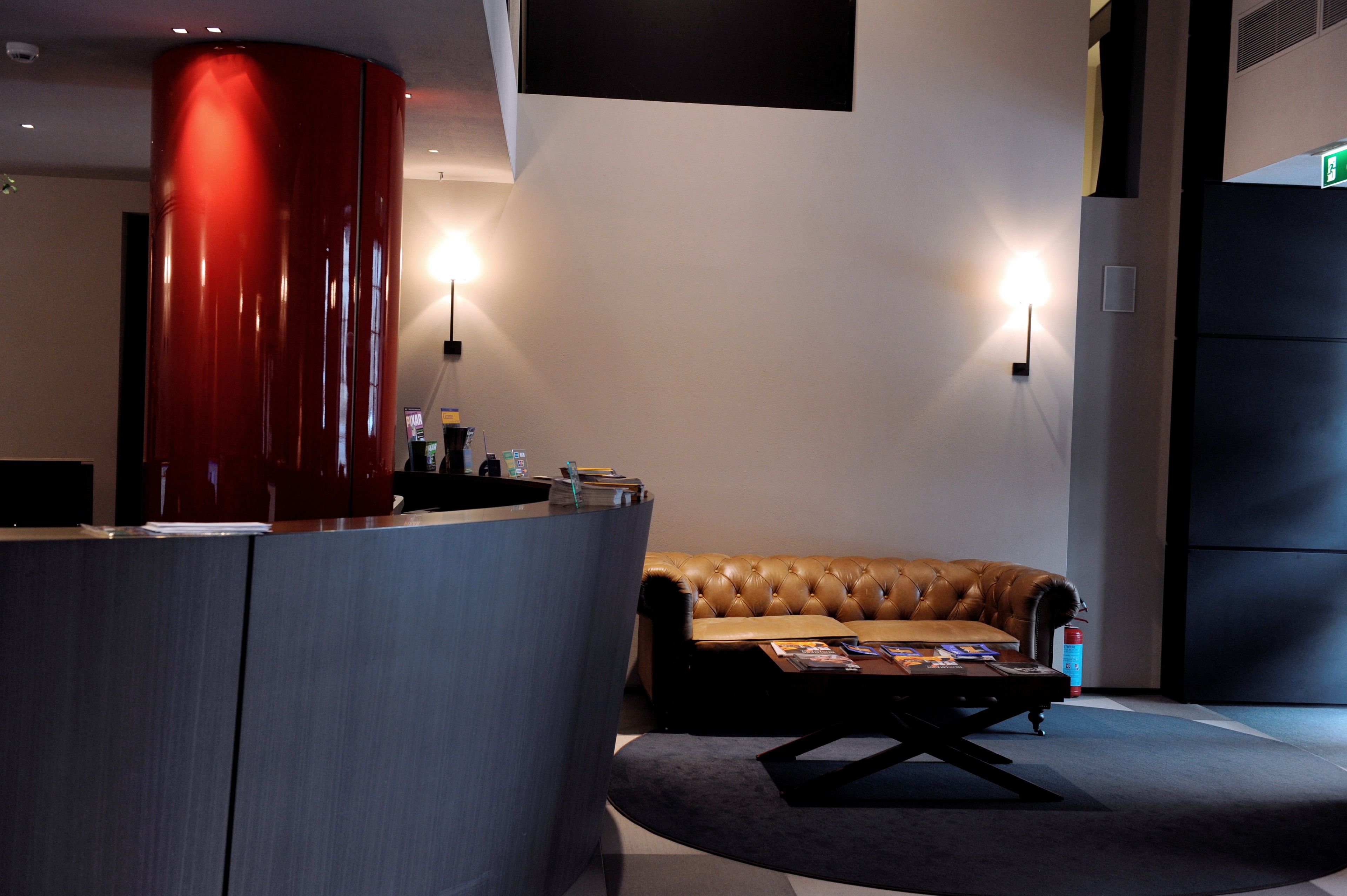 A reception area with a red cylindrical object, a leather couch, and two wall-mounted lights.
