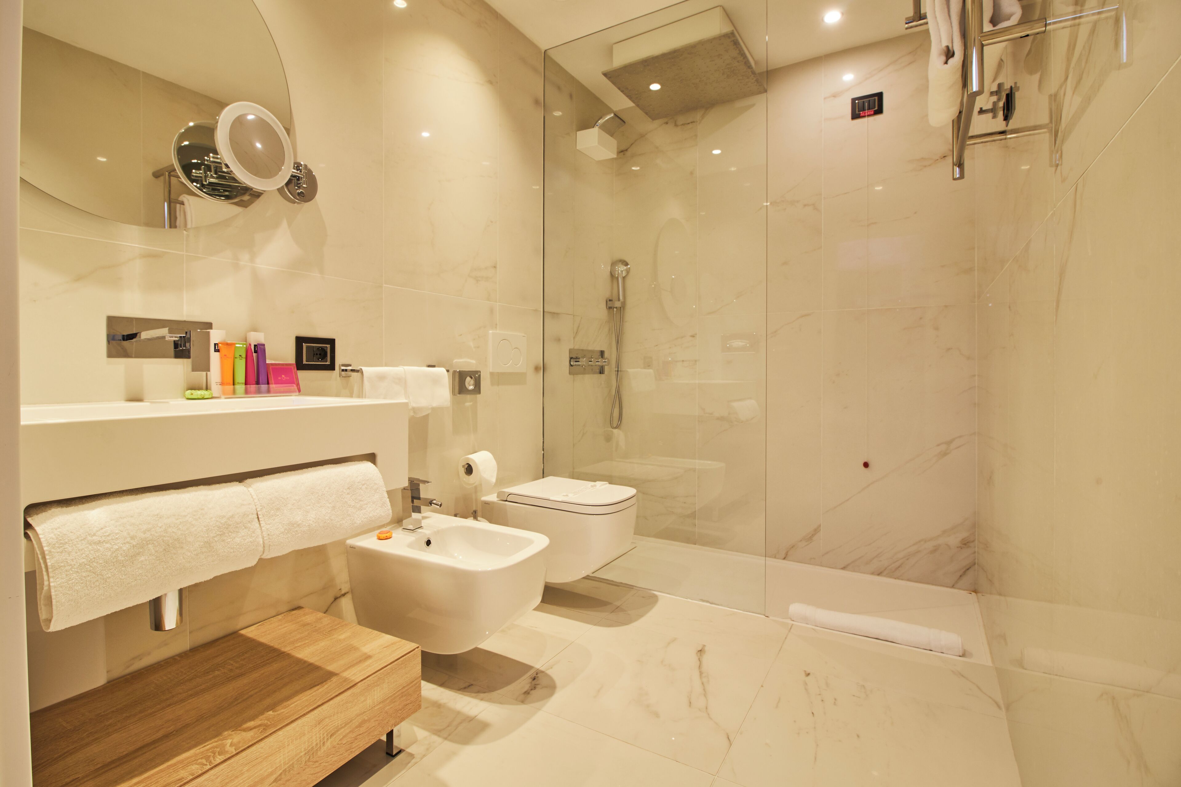 Un baño moderno con ducha envuelta en vidrio, tocador de madera, un bidé y un inodoro.
