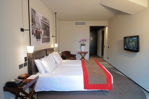 Een hotelkamer met een groot bed, een bureau met telefoon, een stoel, een kleine tafel met een bloevas en een televisie aan de muur.