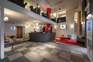 A modern hotel lobby with a checkered floor, a reception desk, and a red accent wall.