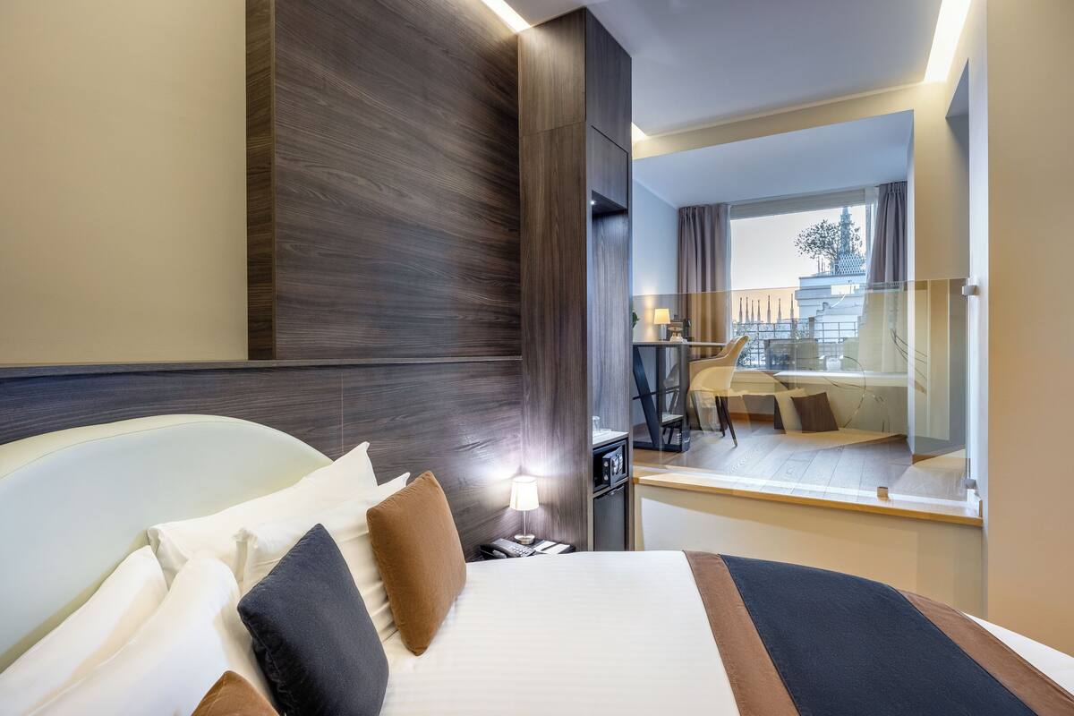 A modern hotel room with a large bed, a desk, and a view of a cityscape.