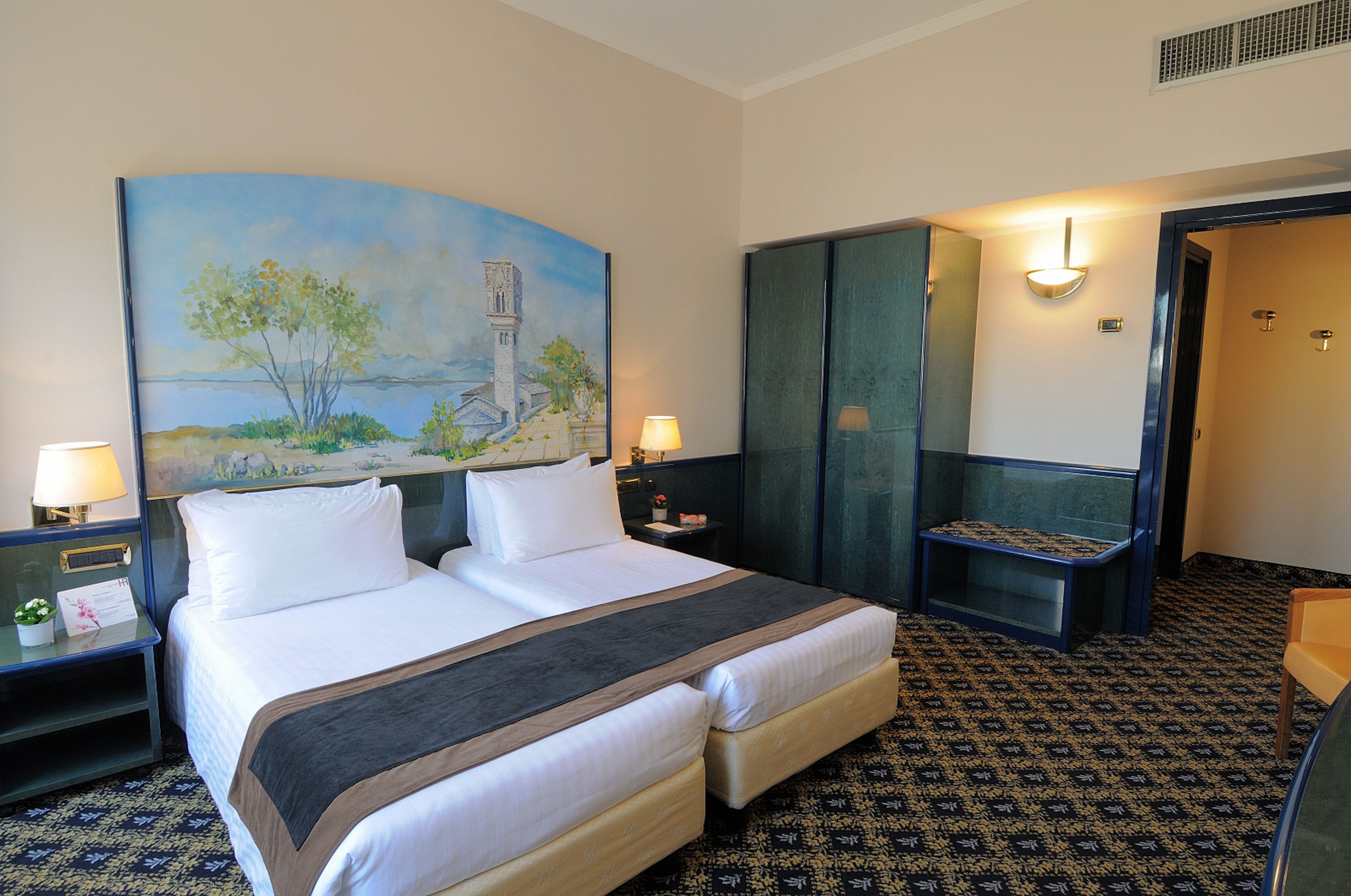 A hotel room with a large bed, two bedside tables, a nightstand, a bench, and a painting on the wall.