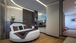 A modern bedroom with a curved bed, a small bedside table, a nightstand, and a potted orchid. - iH Hotels Milano Ambasciatori (Milan)