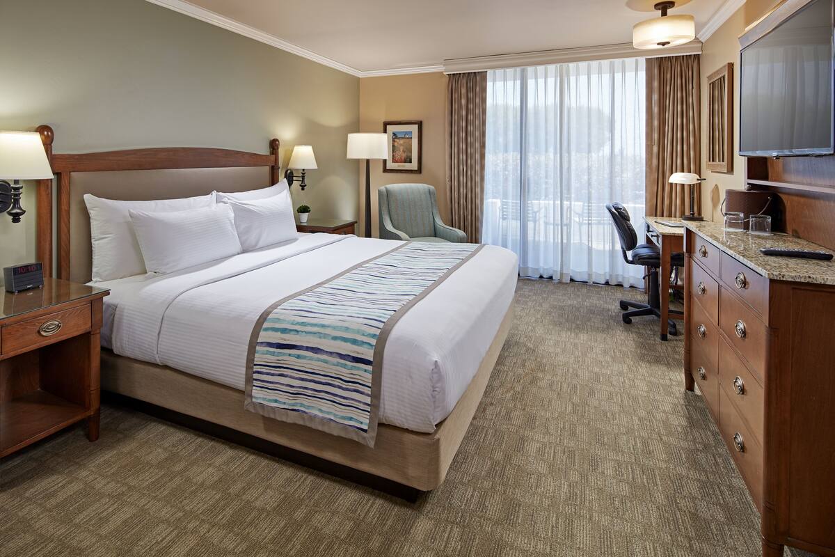 A hotel room with a large bed, a desk, a chair, a dresser, and a TV.