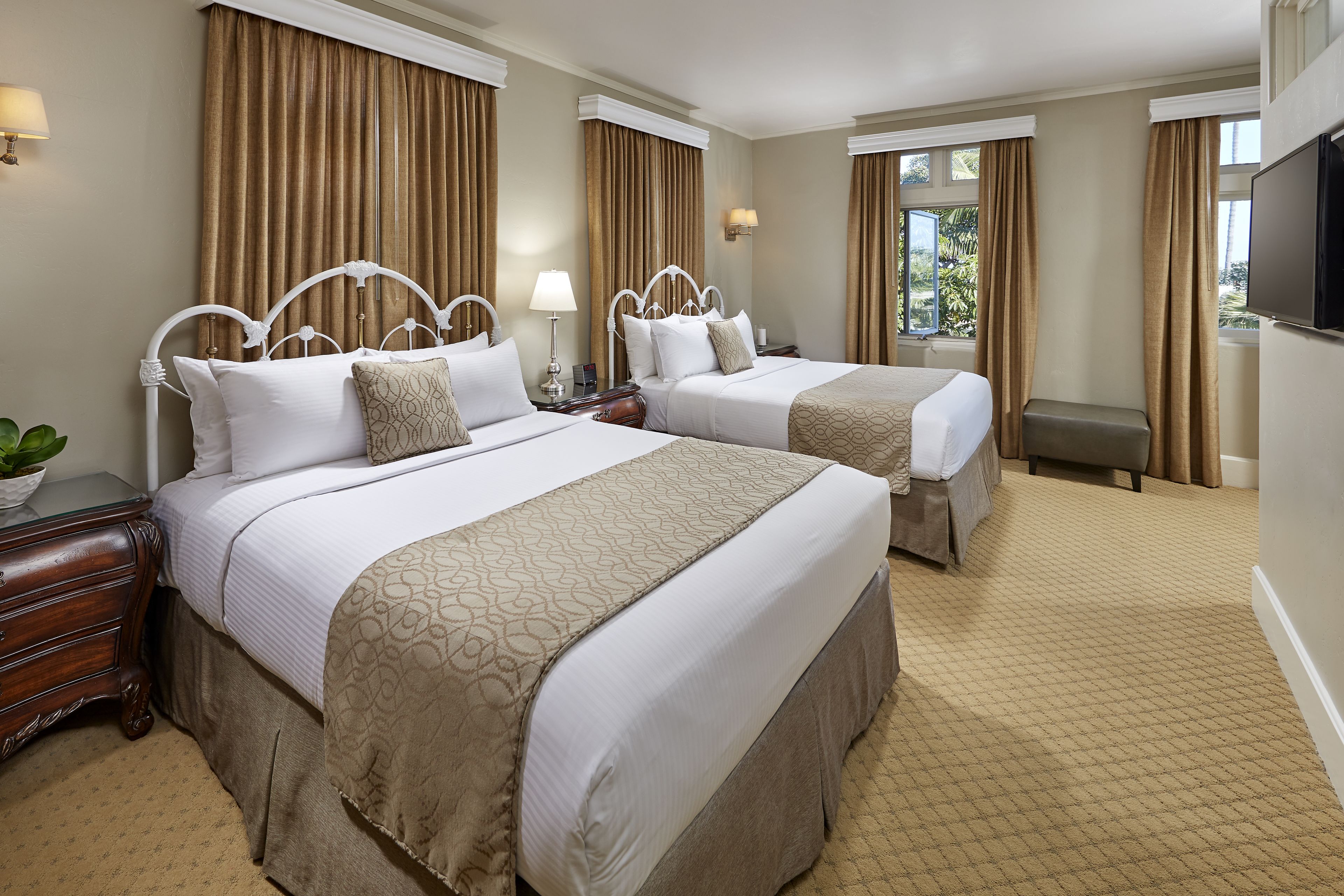 Habitación de hotel con dos camas, televisión, escritorio y ventana con cortinas.