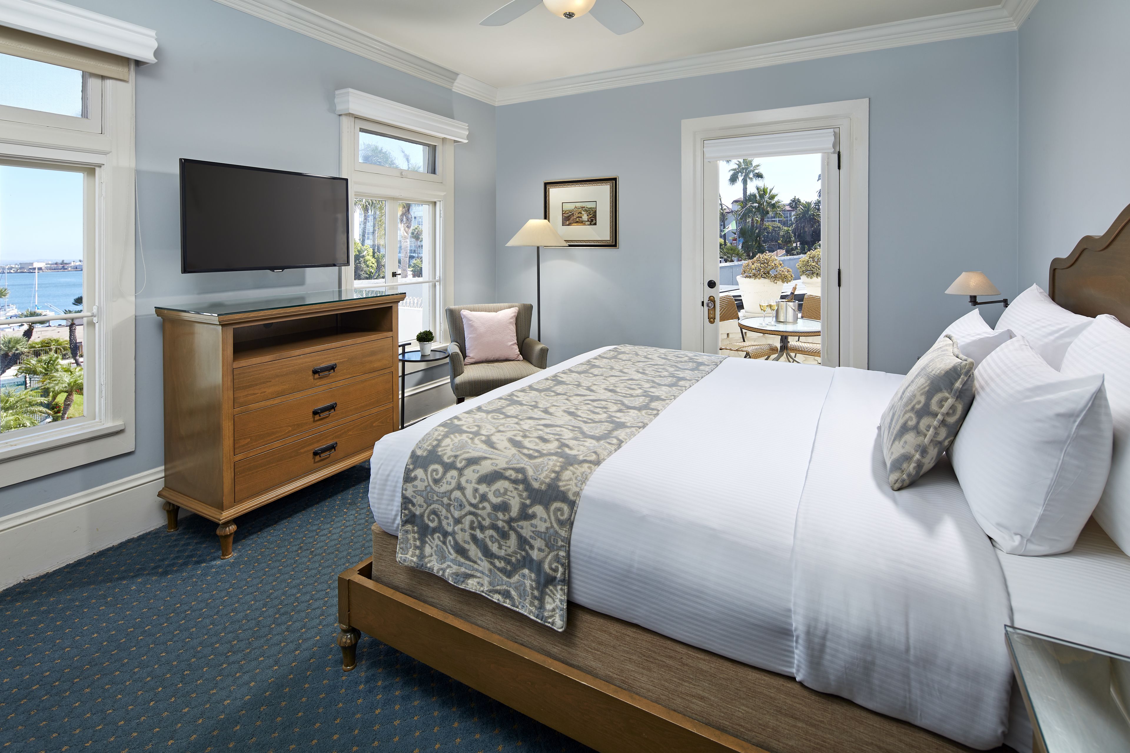 A hotel room with a large bed, a TV, a desk with a chair, and a view of the ocean.
