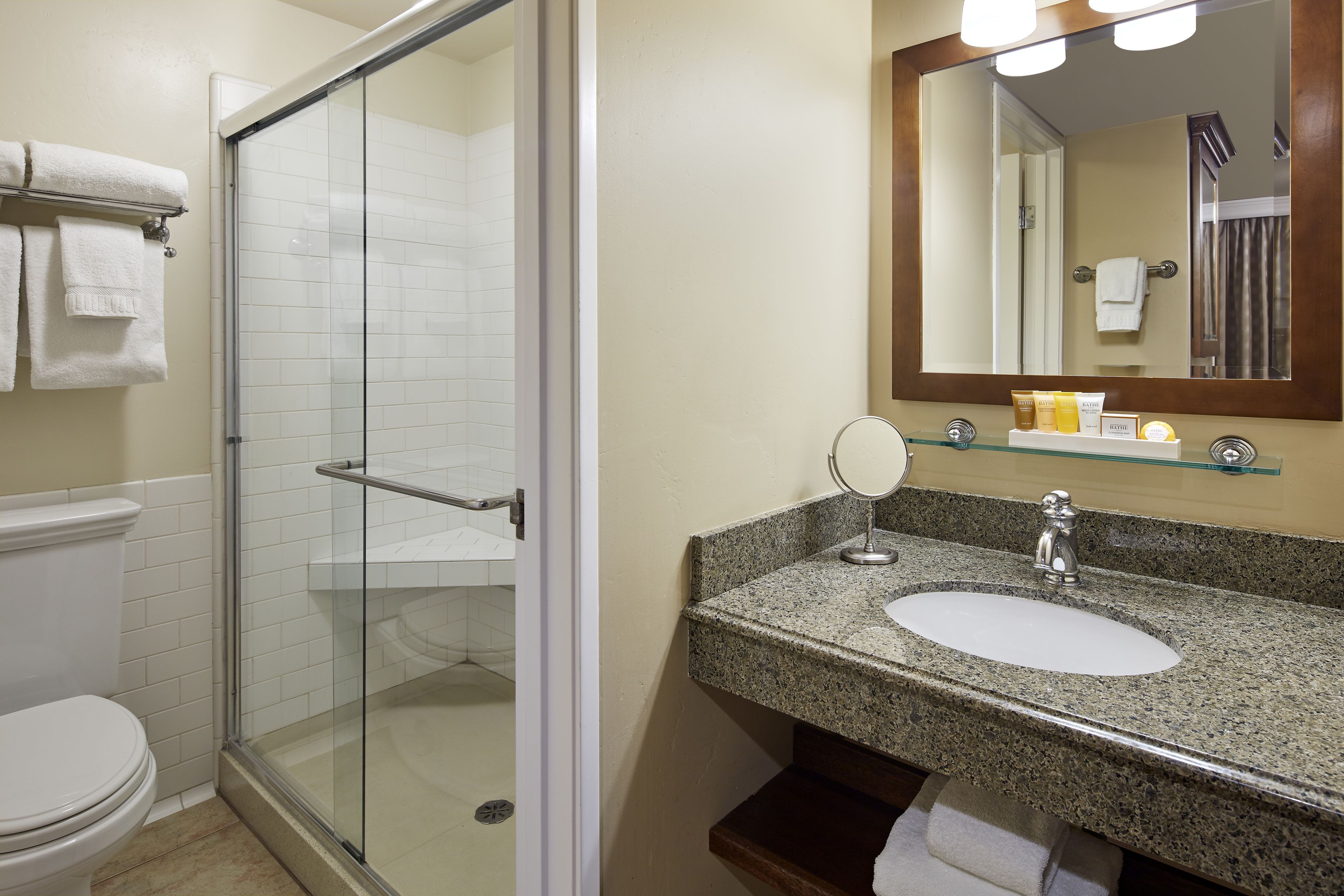 Une salle de bain dotée d’une douche à parois de verre, d’un lavabo blanc avec un plan de travail en granit et d’un miroir au-dessus du lavabo.
