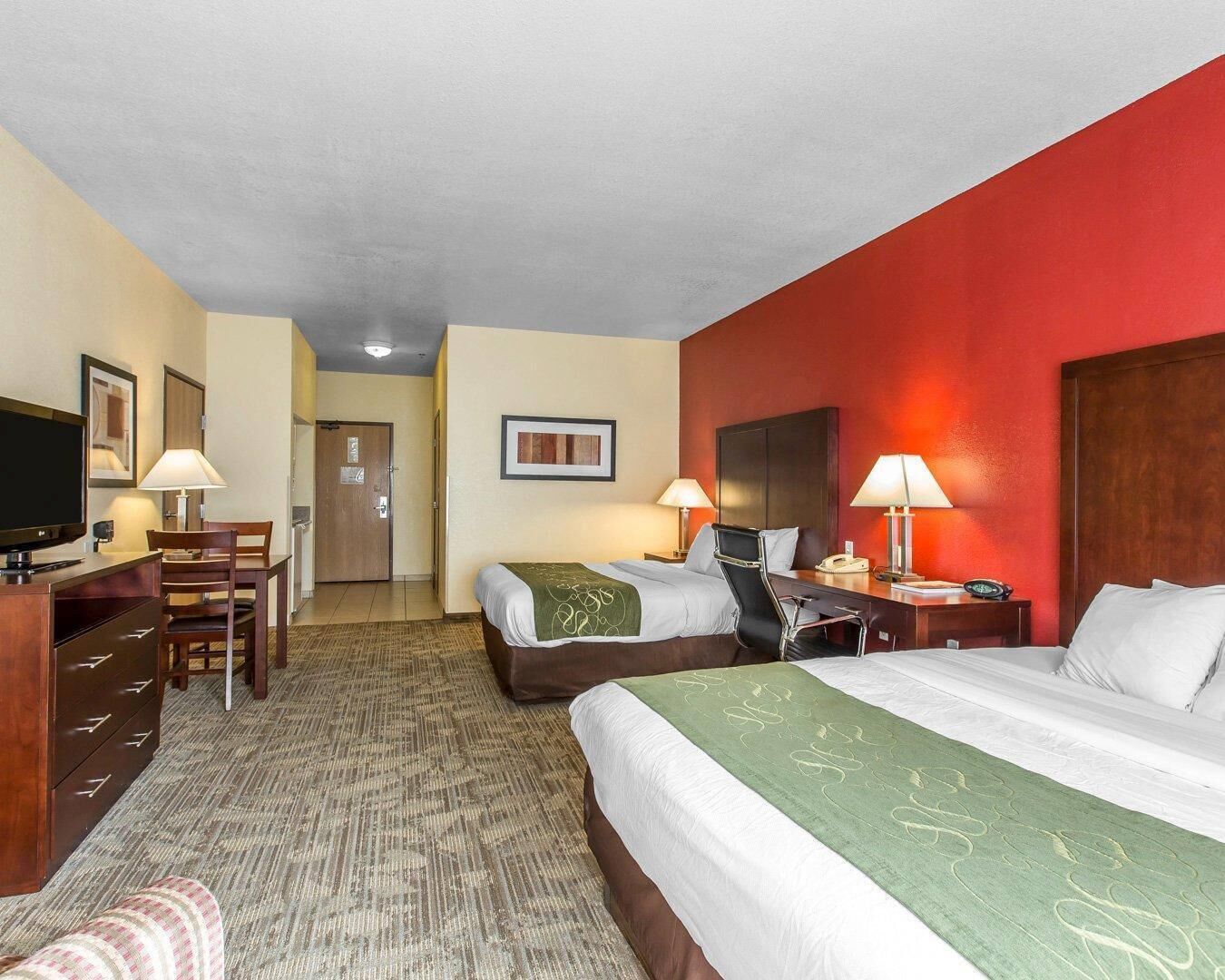 A hotel room with two beds, a desk with a TV, a chair, a desk lamp, and a telephone.