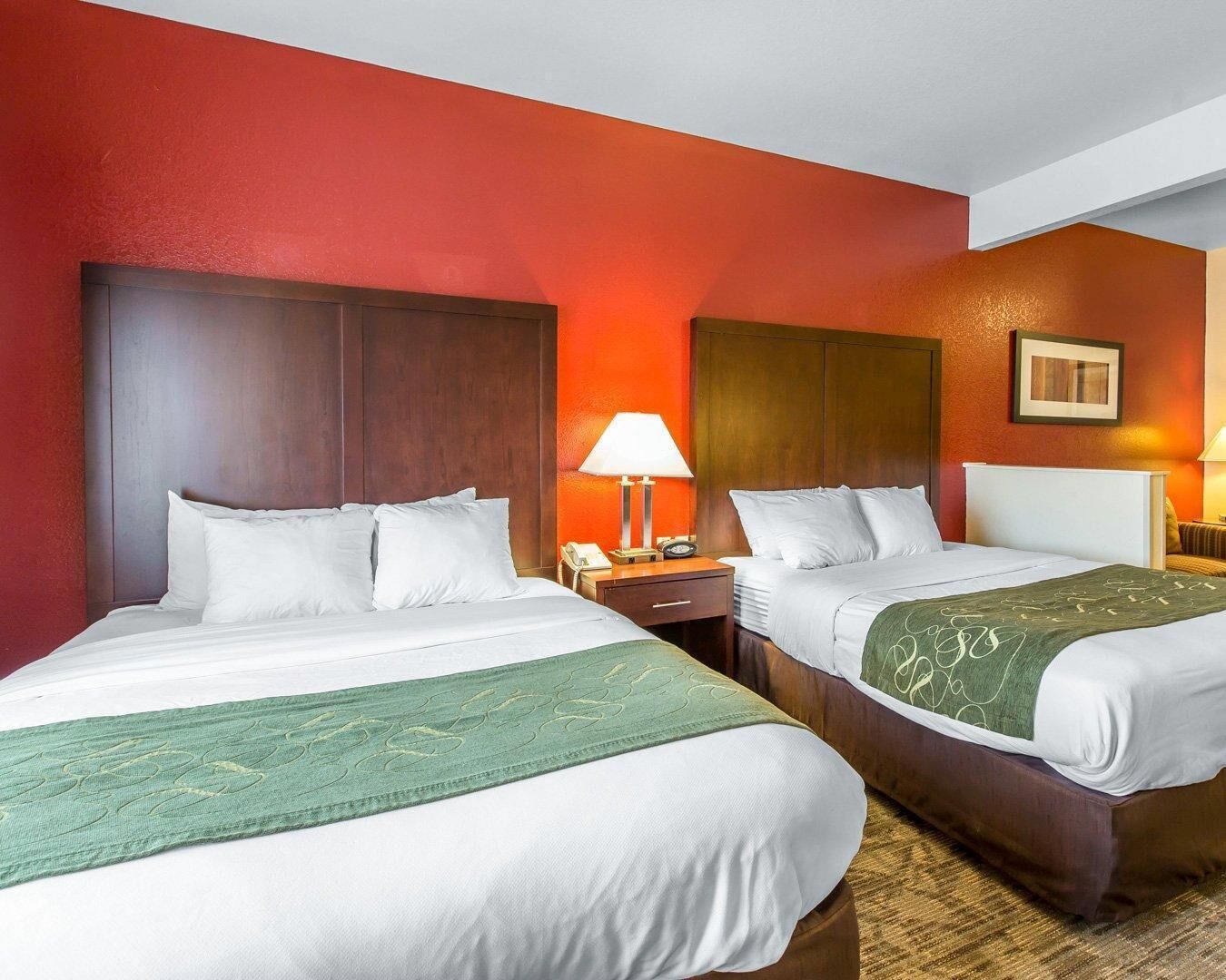 A hotel room with two beds, a nightstand, a lamp, and a framed picture on the wall.