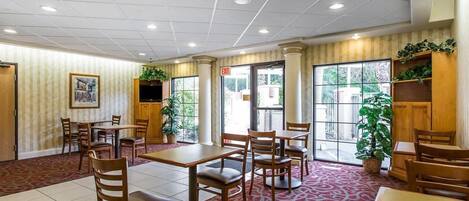 Comedor de hotel con mesas y sillas, un televisor y un amplio ventanal con vistas.