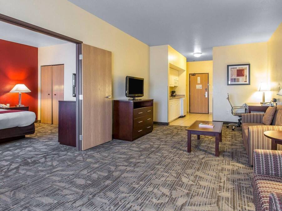 A hotel room with a bed, a TV, a desk, a chair, a sofa, a wardrobe, and a kitchenette.