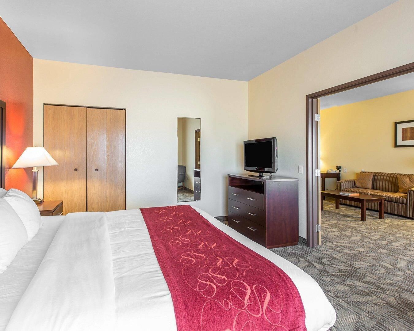 A hotel room with a bed, a TV on a stand, a desk with a chair, and a mirror.