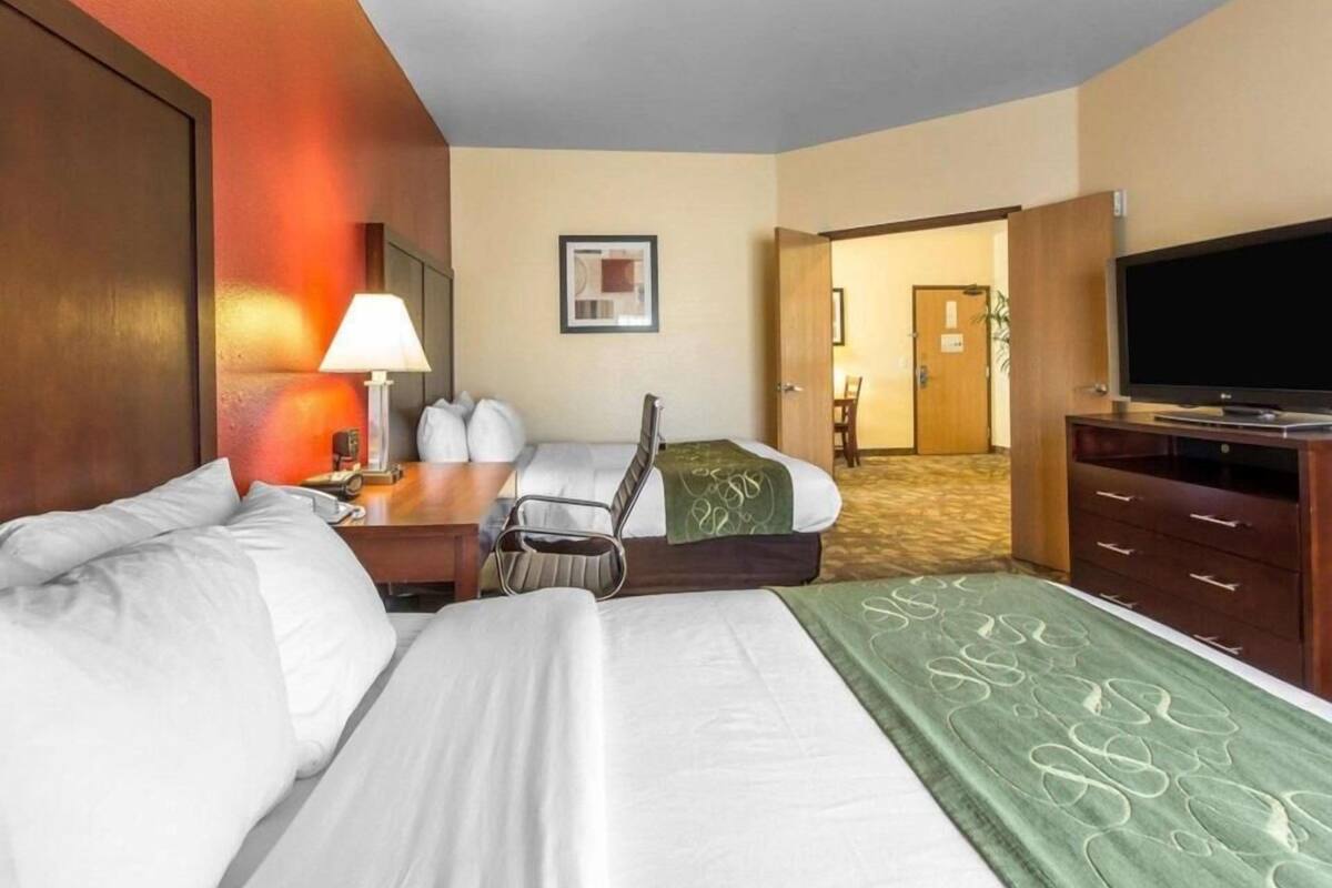 Een hotelkamer met twee bedden, een bureau met lamp, een televisie en een deur naar een andere kamer.