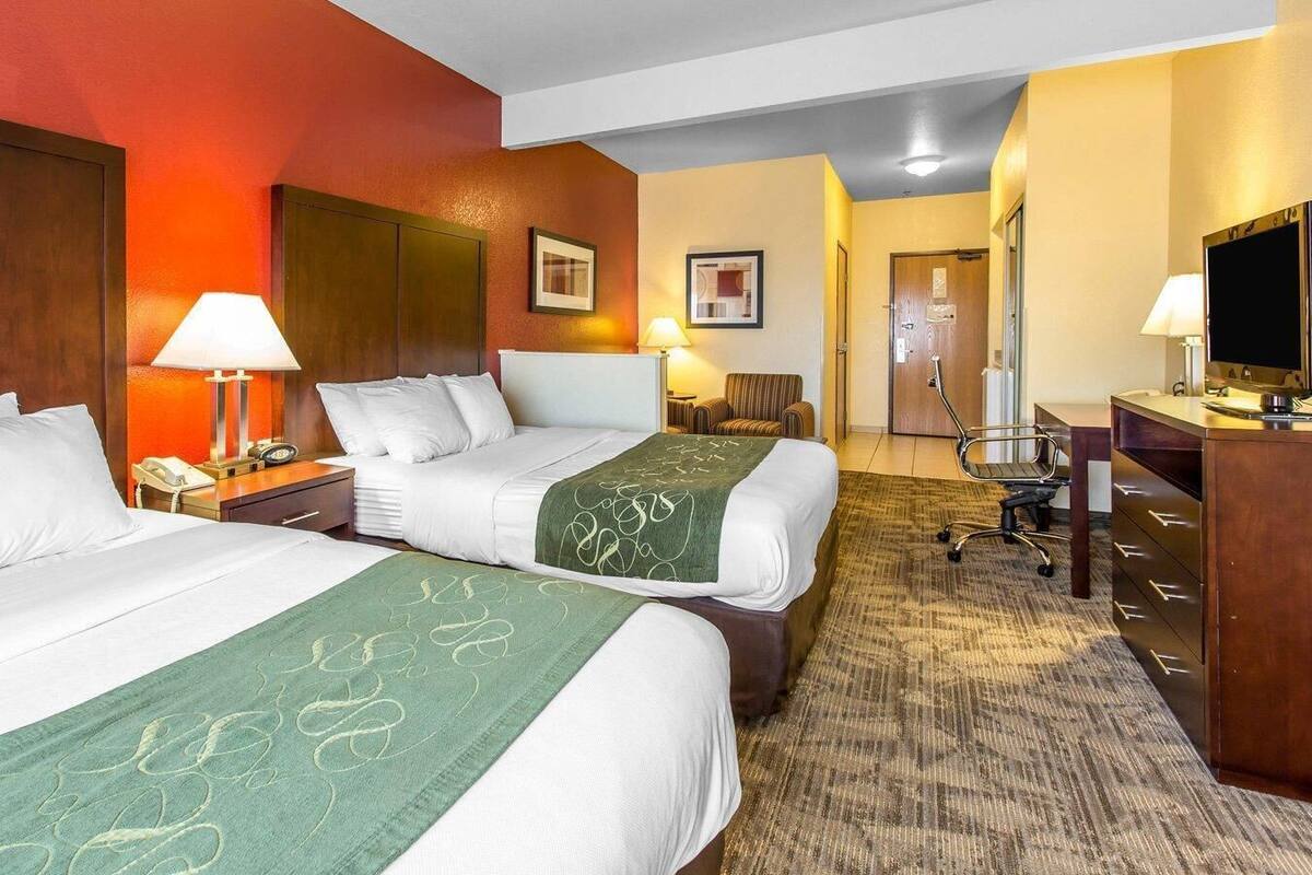 Een hotelkamer met twee bedden, een bureau, een stoel, een televisie en een badkamer die door een open deur zichtbaar is.