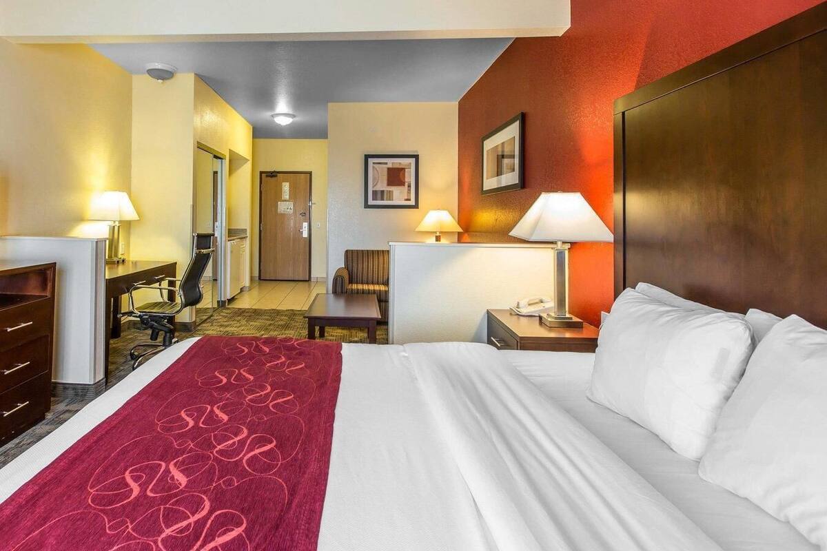 Een hotelkamer met een bed, bureau, stoel en een deur die naar een gang leidt.