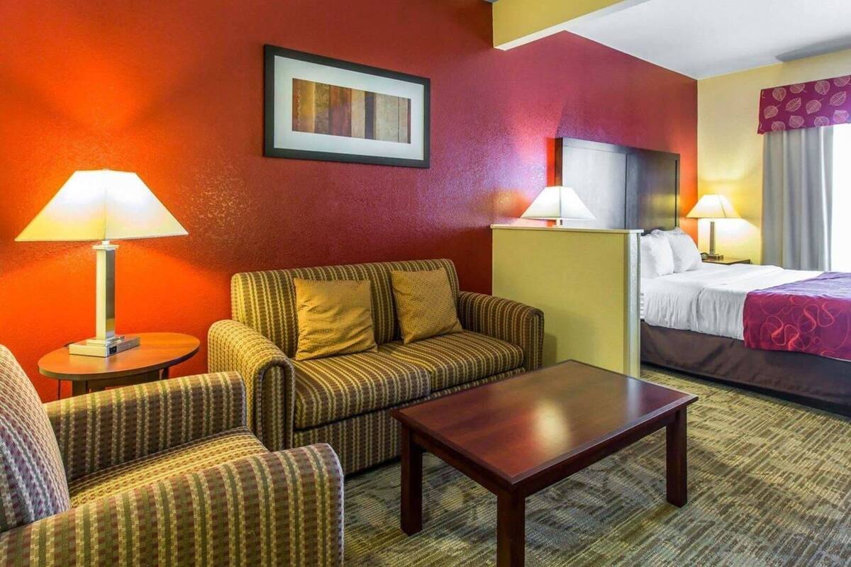Een hotelkamer met een bank, fauteuil en een bed. Er staan lampen op de nachtkastjes.