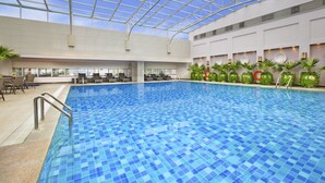 An indoor swimming pool with a glass ceiling, surrounded by lounge chairs and tables. - Sheraton Chengdu Lido Hotel (Chengdu)