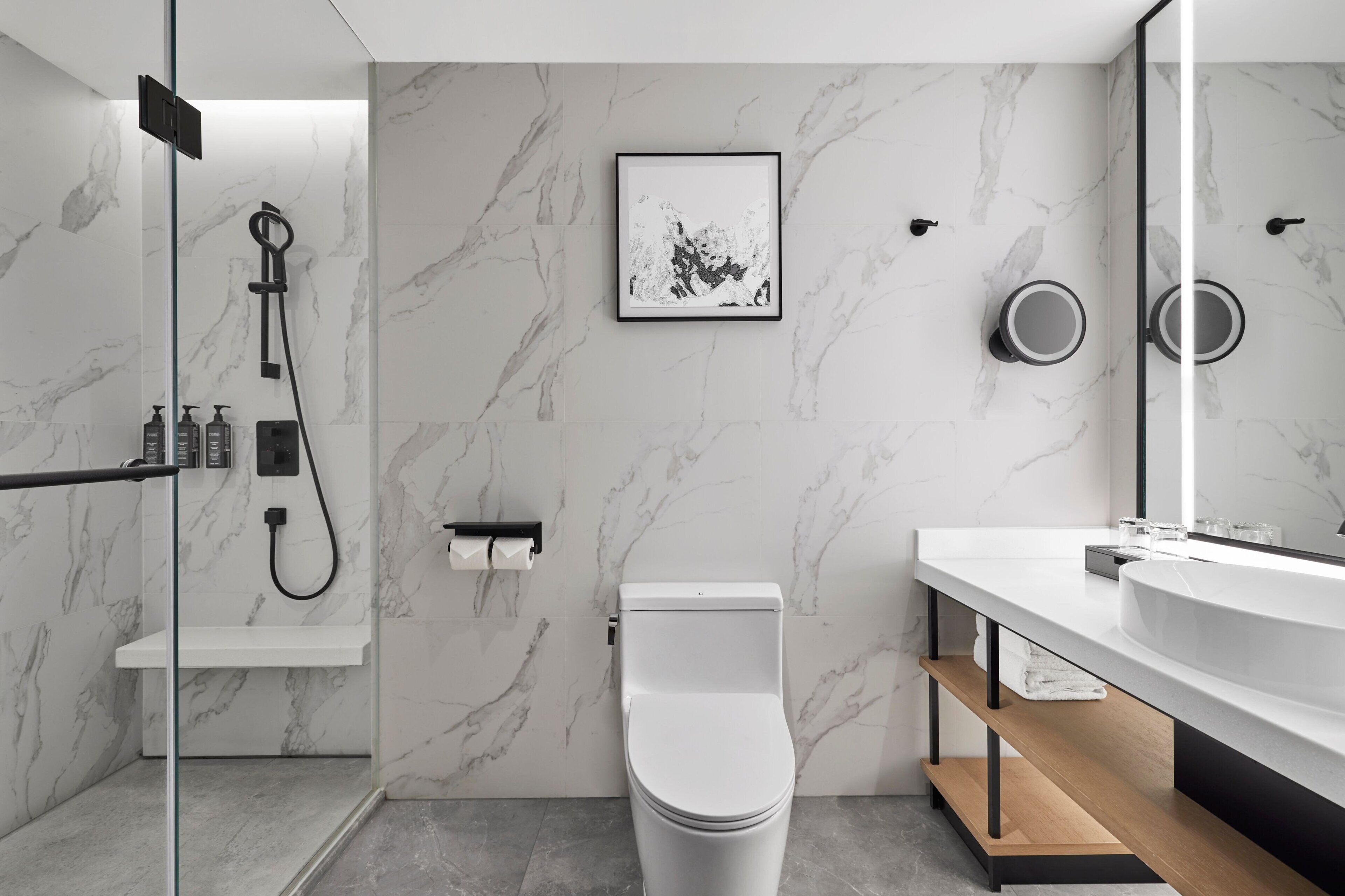 A modern bathroom with a marble backsplash, a toilet, a shower, a sink, and a mirror.