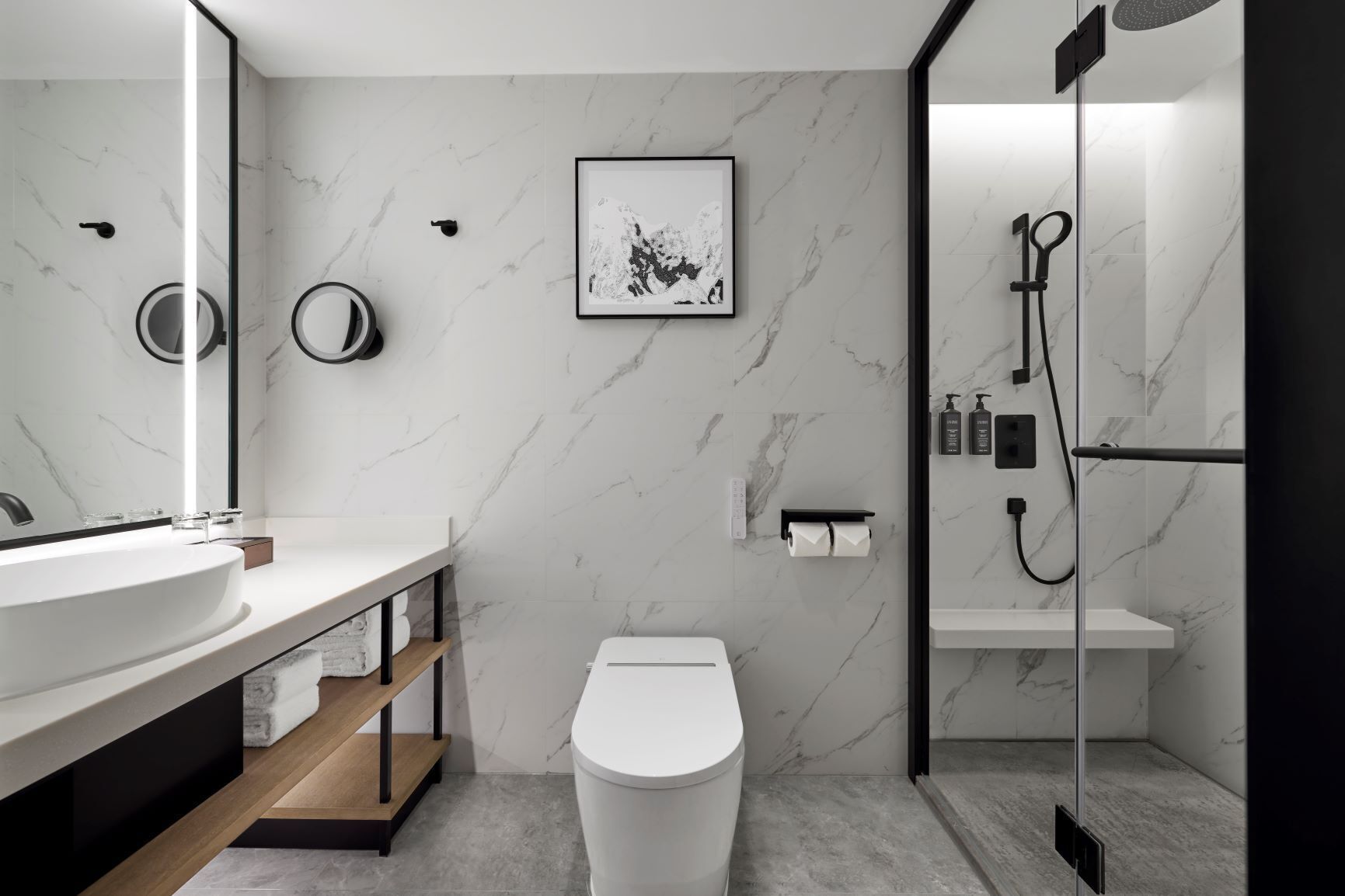 A modern bathroom with a large mirror, a toilet, a shower, and a marble wall.