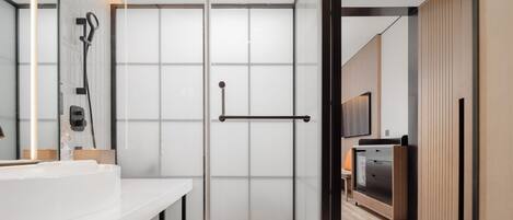 A modern bathroom with a glass shower enclosure, a white sink, and a wooden cabinet.