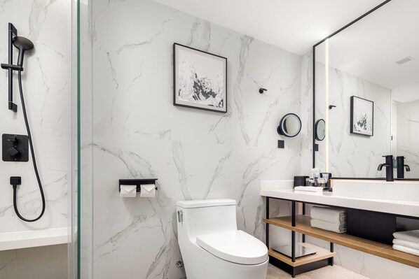Un bagno moderno con un water bianco, una doccia vetrata, una parete in marmo, un lavandino con rubinetto nero e uno specchio.