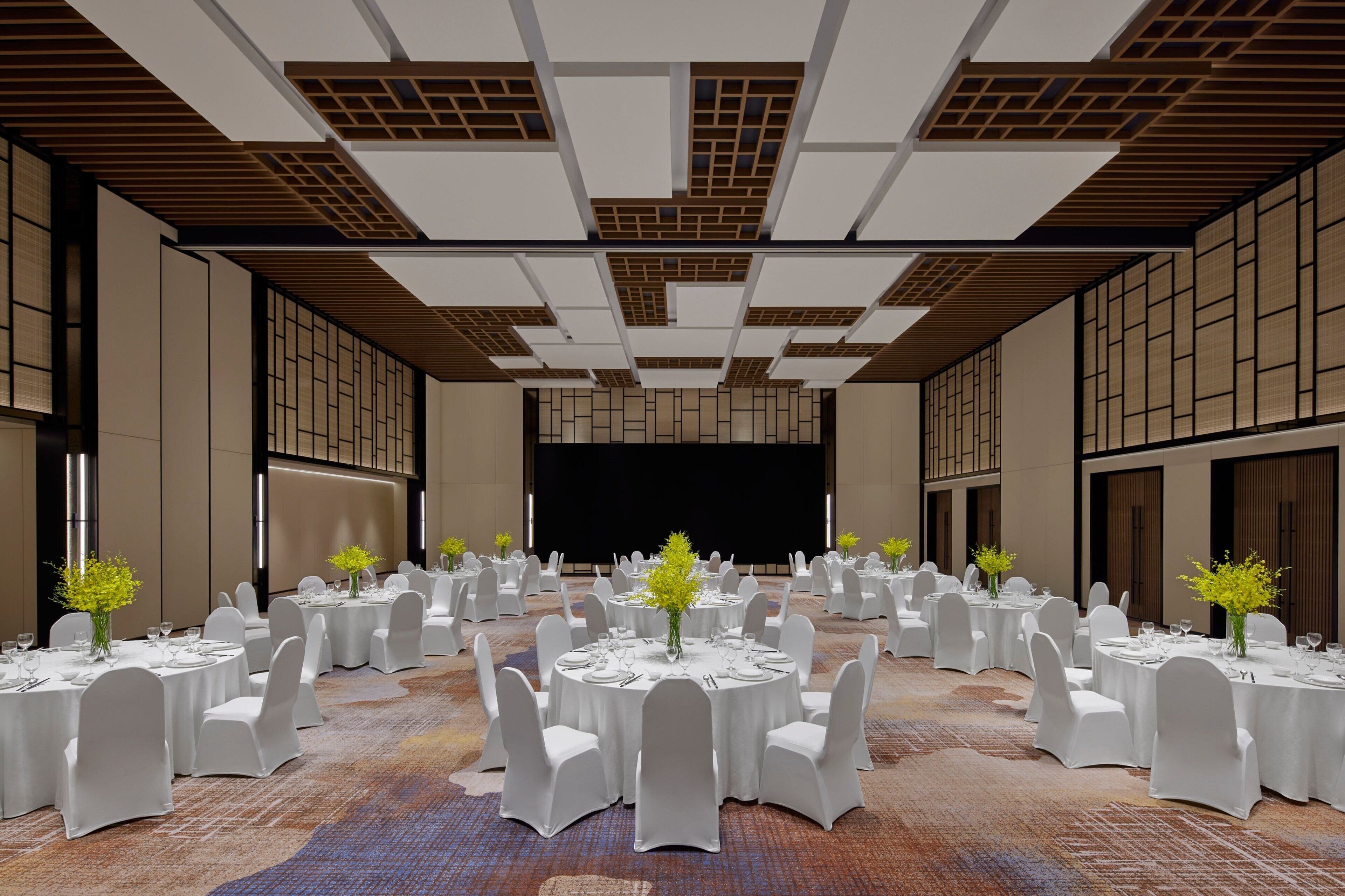 A banquet hall with round tables, white chairs, and floral centerpieces.
