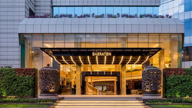 A Sheraton hotel entrance with a modern design, featuring a glass facade, a well-lit entrance, and a landscaped area with steps leading up to the door. - Sheraton Chengdu Lido Hotel (Chengdu)