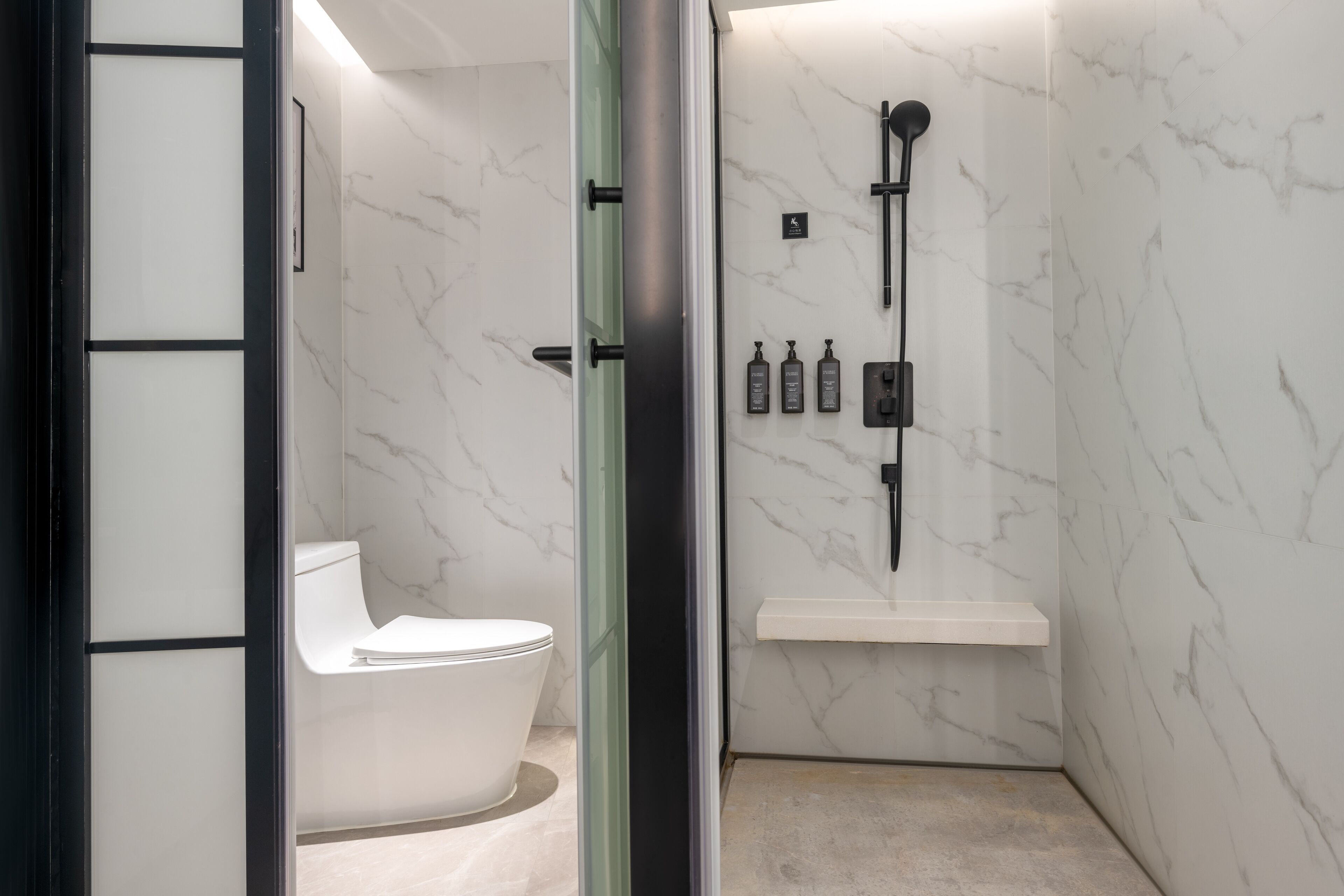 A modern bathroom with a toilet, a shower, and a marble wall.