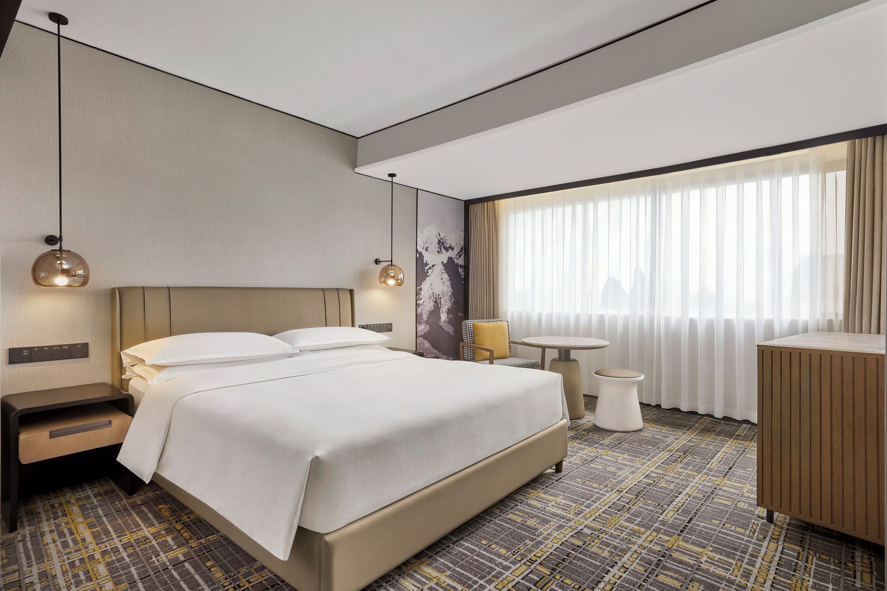Una habitación de hotel con una cama grande, mesitas de noche, un escritorio pequeño y una ventana con cortinas.