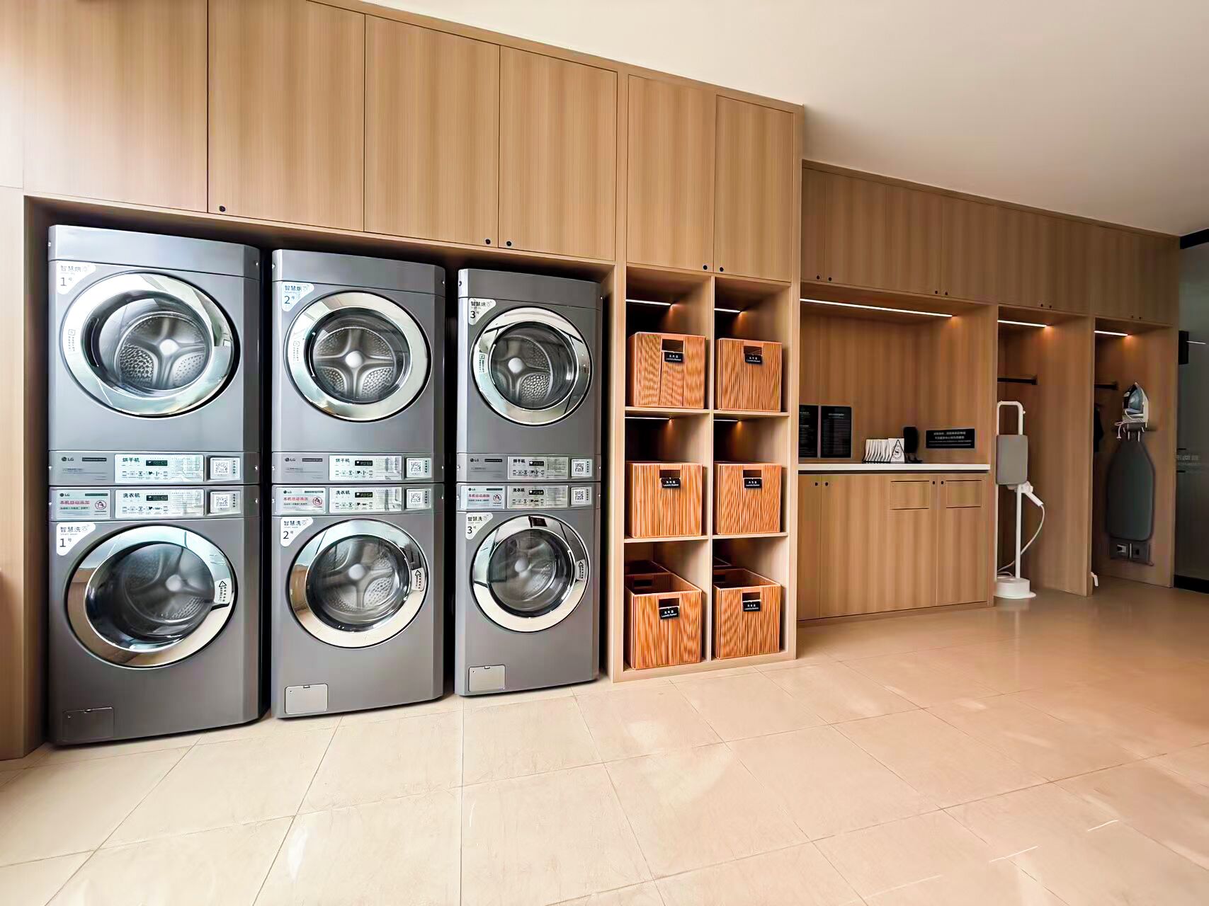 Una lavandería moderna con cuatro lavadoras apiladas, estanterías de madera y un aspirador.