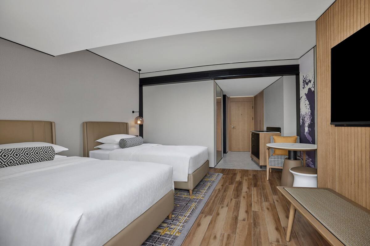 A hotel room with two beds, a small sitting area, a desk, and a TV.