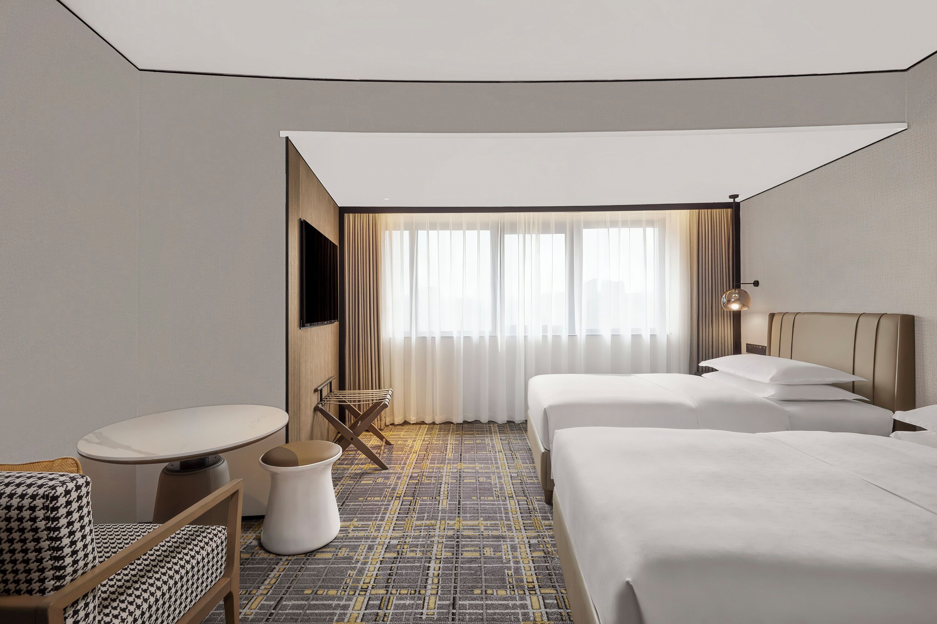 Habitación de hotel con dos camas, una mesita, una silla y un televisor.